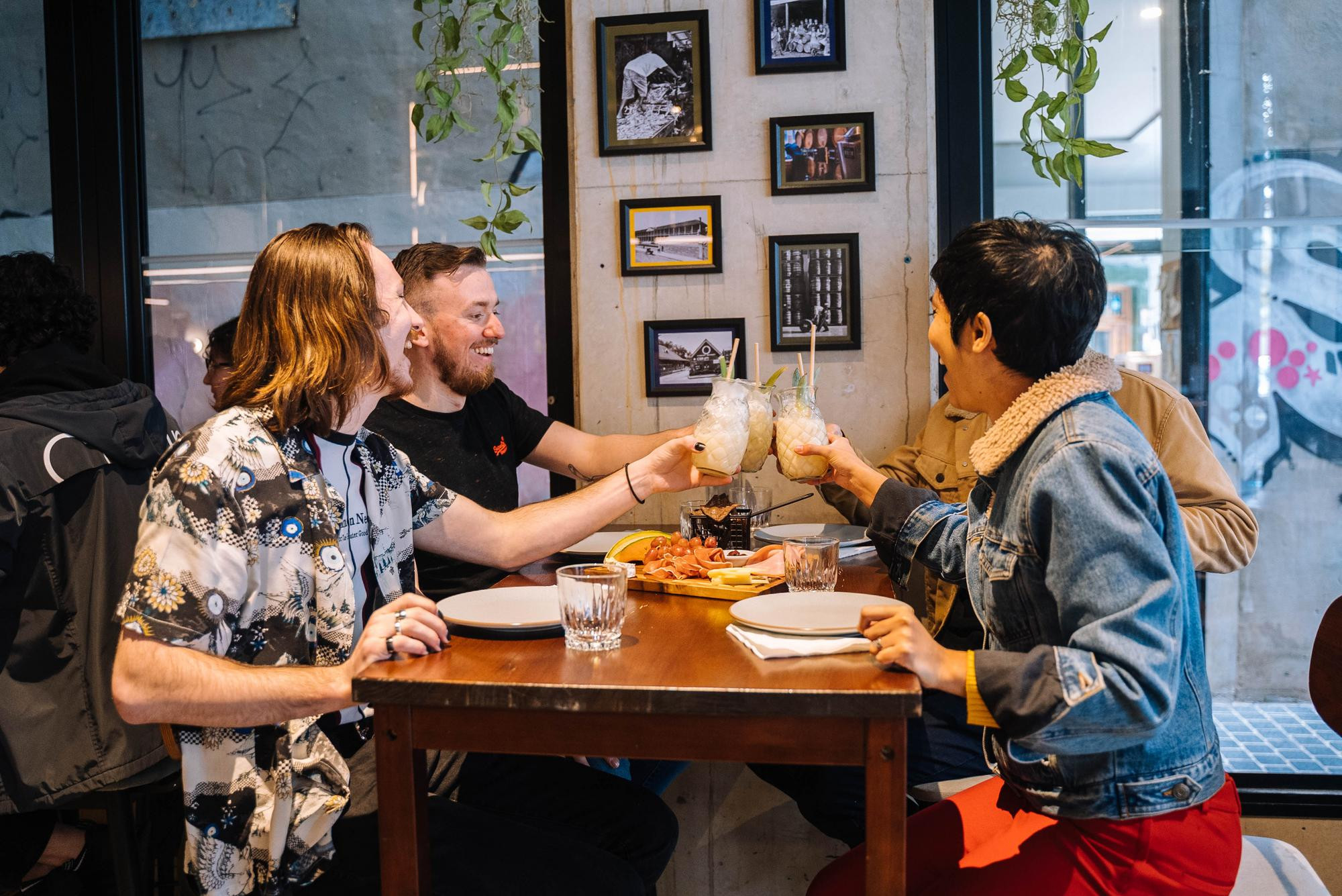 Three smiling people sitting at a table, toasting with pineapple shaped glasses of cocktail